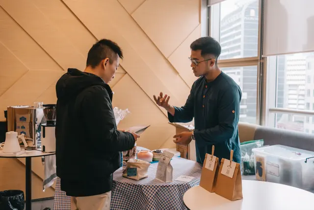 A Brewprint barista talking a guest through the coffees, with bags of beans on the table between them