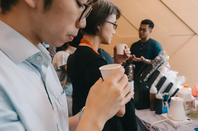 Guests sipping from small tasting cups while a Brewprint barista explains the coffee behind the bar