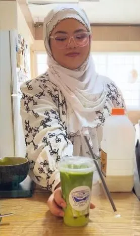 An iced matcha latte in a Brewprint cup held up to the camera