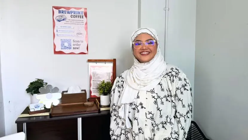 Brewprint co-founder smiling beside the café’s scan-to-order poster and menu board