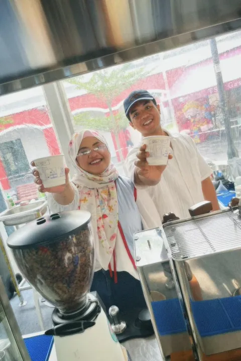 Two of the Brewprint team smiling and raising Brewprint cups behind the grinder and espresso machine